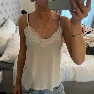 Vit spetslinne från Amisu - Säljer en ljusvit linnetopp från Amisu i storlek XS. Toppen har tunna axelband och v-ringad hals med snygga spetsdetaljer framtill. Materialet är mjukt och lent, perfekt för en chill och stilren look. Passar dig som gillar enkla men fina detaljer.