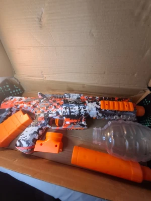 Elektrisk Gel Blaster med USB-laddning - Elektrisk gel blaster med färgstark orange/svart/vit camo-design. Levereras med USB-laddkabel och avtagbart magasin. Utrustad med stor behållare för gelkulor. Produkten ser ut att vara i gott skick utan synligt slitage eller defekter.