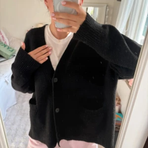 Svart oversized kofta från Monki - Svart, mysig och oversized kofta från Monki med två stora fickor framtill och ribbade muddar. Koftan har v-ringning, knappar och är långärmad. Perfekt för lager-på-lager och chill dagar. Materialet är stickat och ger en skön känsla.