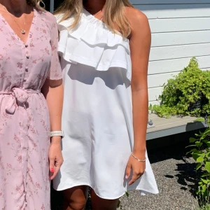 Vit oneshoulder klänning med volang - Supersöt vit kortklänning med oneshoulder och bred volang upptill. Klänningen är perfekt till student och sommar!🌸