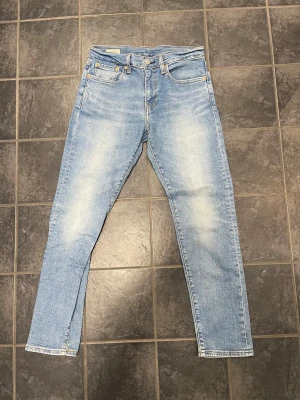 Ljusblå Levi's 512 Jeans Straight Fit - Säljer nu dessa snygga ljusblå Levi's 512 jeans med klassisk femficksdesign och raka ben. Jeansen har en snygg tvätt med lätt slitning på framsidan och den ikoniska läderpatchen bak i midjan. Passar dig som gillar tidlös och clean stil. Byxorna är i storlek 28/30.