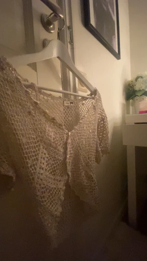 Beige virkad bolerotopp från Joy - Superfin beige bolerotopp från a feeling of Joy, virkad med glittriga paljettdetaljer. Croppad modell med korta ärmar och v-ringad framkant. Perfekt att slänga över en klänning eller linne för en extra touch. Hör ba av för fler frågor💞💞