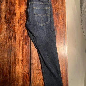 Mörkblå jeansbyxor Pistolero 29/32 - Snygga mörkblå jeansbyxor från Pistolero med klassisk femficksdesign och kontrastsömmar. Modellen har rak passform och läderpatch bak i midjan. Tillverkade i robust denim med gul söm för en cool look.