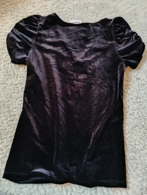 Svart sammetsblus med puffärm Kappahl - Snygg svart blus från Kappahl i mjuk sammet. Modellen har korta puffärmar och en djup v-ringning framtill. Perfekt för dig som gillar en stilren look med lite extra lyxig känsla. Passar dig som vill ha något som sticker ut men ändå är enkelt att matcha. Nästan helt oanvänd.