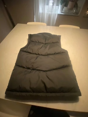 Svart väst med dragkedja  - Snygg svart väst  med hög krage och praktisk dragkedja framtill. Västen har två stora fickor på sidorna och quiltad design som ger en cool look. Perfekt att slänga över en hoodie när det är kyligt ute. Väldigt Grisch oxå