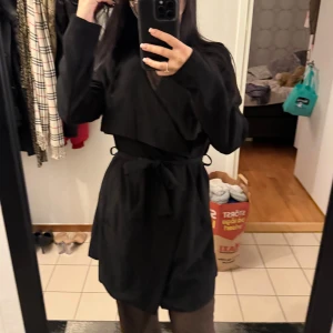 Svart trenchcoat med bälte - Säljer en svart trenchcoat med snygg omlott-design och knytbälte i midjan. Jackan har långa ärmar och en stilren, klassisk look som passar perfekt till höst och vår.  Aldrig använd!! 