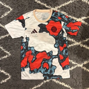 Bayern München fotbollströja  - Säljer en FC Bayern München fotbollströja från Adidas i slim fit. Tröjan har korta ärmar och är tillverkad i lätt polyester. Färgen är vit med stora röda och mörkblå mönster, samt beige krage. Klubbmärket och Adidas-loggan syns tydligt på bröstet. Jag är 180cm, 68kg och den sitter bra på mig.