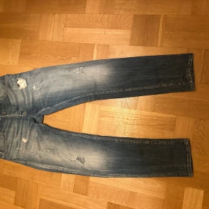 Replay RBJ 901 blå jeans, storlek 32 - Snygga Replay RBJ 901 jeans i blå tvätt med slitningar och distressed detaljer. Klassisk femficksmodell med raka ben och normal passform. Jeansen har ljusare partier och coola revor framtill, tillverkade i mjukt bomullsmaterial.