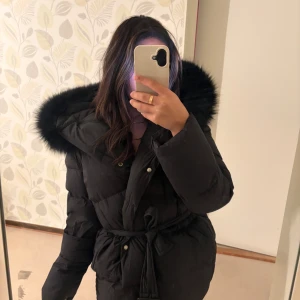 Svart dunjacka med pälsluva och bälte - Säljer min vinterjacka från Fur Stockholm. Jackan är i jättefin och nästantill nyckick. Jag föredrar längre modeller under vintern och väljer därför att sälja denna. Denna är perfekt för dig som vill ha en varm och stilren vinterjacka i kort modell. Jackan är väldigt omtyckt och populär. Pris kan diskuteras vid snabb affär.