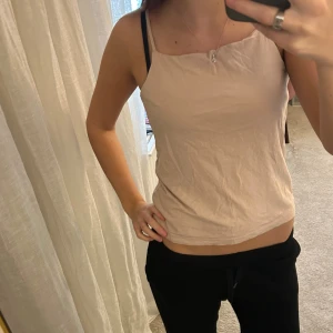 Beige/rosa  linnetopp med smala axelband - Säljer en enkel och stilren beige linnetopp med smala axelband. Toppen har rak halsringning och är ärmlös, vilket gör den perfekt för varma dagar. Materialet känns lätt och luftigt mot huden. Passformen är normal och toppen är lätt att matcha med olika outfits.