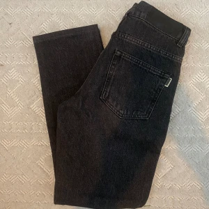Oanvända Svarta jeans från Woodbird - Snygga svarta jeans från Woodbird med klassisk femficksdesign och svart patch bak i midjan. Jeansen har raka ben och är tillverkade i ett robust jeanstyg som ger en cool och tidlös look. Perfekta för dig som gillar stilrena och enkla jeans. Storlek 27/30. Nypris 1200kr