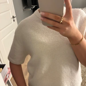 Vit stickad tröja från Gina Tricot - Säljer en vit stickad tröja från Gina Tricot i ullblandning. Tröjan har korta ärmar, rund hals och ribbade kanter vid ärmslut och nederkant. Modellen är loose fit och har en mjuk, lite fluffig yta som känns riktigt skön mot huden.