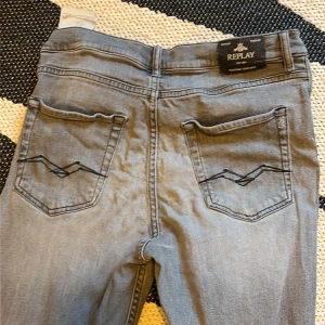 Replay ljusgrå jeans med broderade fickor - Snygga ljusgrå jeans från Replay med klassisk femficksdesign och svarta broderade detaljer på bakfickorna. Jeansen har knappstängning och bälteshällor, perfekt för dig som gillar stilrena och coola jeans. Passar dig som är ca 158 cm lång.