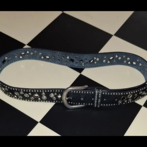 Svart bälte - Snyggt svart bälte med massor av silvriga   stora metallhål längs hela bandet. Bältet har en robust silverspänne och coola detaljer som ger en edgy vibe. Perfekt accessoar för att lyfta din outfit med lite extra attityd.