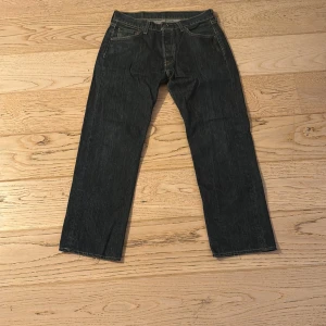 Levi's 501 jeans mörkblå W29 L30 - Klassiska Levi's 501 jeans i mörkblå denim med raka ben och femficksmodell. Snygga kontrastsömmar och ikonisk läderpatch bak i midjan. Perfekt för dig som gillar tidlös stil och vill ha ett par jeans som funkar till allt.