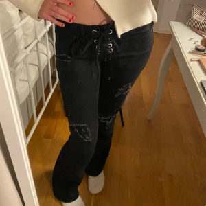 Snygga svarta jeans med snörning  - Svarta jeans med låg midja och snörning framtill. Byxorna har slitna detaljer på benen. Snygg passform och coola detaljer! Storlek Xs. Använt 1 gång.