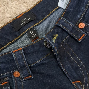True Religion Joey Low Rise Flare Jeans - Mörkblå jeans från True Religion, modell Joey Low Rise Flare. Snygga kontrastsömmar i orange och gult, klassiska fickor med dekorativa sömmar och logoknappar. Låg midja och utsvängda ben ger en cool retrostil. Använda en gång pris kan diskuteras ❤️💕