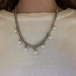 Silverfärgat halsband med pärlor - Snyggt halsband i silverfärgad kedja med hängande vita pärlor. Kedjan är lite chunky och pärlorna ger en elegant touch. Perfekt accessoar för att lyfta din outfit. Handgjort