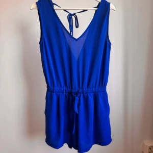 Kort jumpsuit/playsuit i blått - En fin blå kort jumpsuit från Sisters Point i storlek XS. Fickor på sidorna. Använd fåtal gånger och är därmed i bra skick. Bilden matchar färgen i verkligheten.