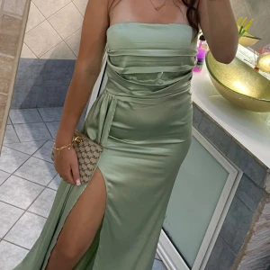 Ljusgrön axelbandslös långklänning - Snygg axelbandslös långklänning i ljusgrönt satinliknande material. Klänningen har draperad överdel, markerad midja och en hög slits på ena benet. Perfekt för dig som vill sticka ut med en elegant och trendig look. Används på ett bröllop fick många komplimanger perfekt för en bal klänning också rekommenderas verkligen🤩