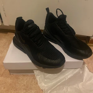 Nike Air Max 270 svarta sneakers - Svarta Nike Air Max 270 sneakers med chunky sula och synlig Air-enhet i hälen. Ovandelen är i mesh och syntet med snörning och rund tå. Snygg, sportig look som passar perfekt till streetwear. Levereras i originalkartong. (Väldigt mycket använda) 