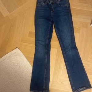 Blå bootcut jeans med normal passform - Snygga blå jeans med bootcut-modell och klassisk femficksdesign. Jeansen har en normal passform och är tillverkade i ett mjukt denimtyg som ger en skön känsla. Perfekta för dig som gillar en tidlös stil med lite utsvängda ben.