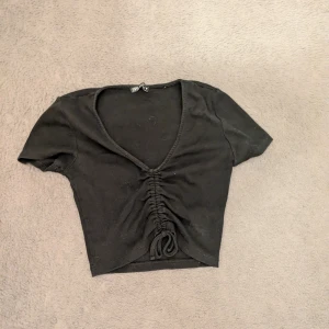 Svart croppad topp med snörning - Svart croppad topp från Zara med korta ärmar och snygg v-ringning. Toppen har snörning framtill som ger en cool rynkad effekt och gör att du kan justera passformen. 