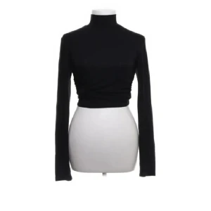 Svart croppad polotopp - Snygg svart croppad polotopp med lång ärm och hög krage. Perfekt för att skapa en clean och stilren look. Toppens tighta passform och minimalistiska design gör den enkel att matcha med både jeans och kjol.