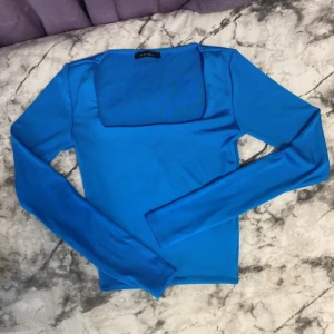 Blå långärmad topp från Amisu - Snygg blå långärmad topp från Amisu från butiken new yorker  med fyrkantig urringning. Toppens material är stretchigt och mjukt, perfekt för att skapa en clean och stilren look. Passar dig som gillar färg och enkel design.