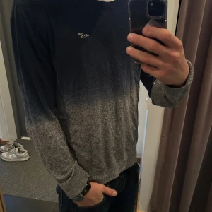Mörkblå-grå tröja från Hollister - Snygg tröja från Hollister i storlek L med mörkblå upptill och grå nertill i en snygg gradient. Tröjan har rund hals, långa ärmar och ett litet Hollister-logo broderat på bröstet. Perfekt för dig som gillar stilrena och bekväma plagg.