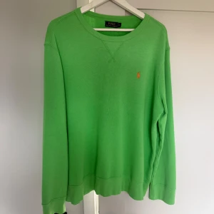 Grön sweatshirt från Polo Ralph Lauren - Fräsch grön sweatshirt från Polo Ralph Lauren i storlek XL. Tröjan har rund hals, lång ärm och en liten orange broderad logga på bröstet. Mjuk bomullskvalitet och klassisk passform som är chill och enkel att matcha med jeans eller shorts.