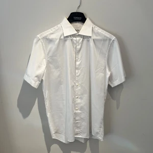 Vit kortärmad skjorta från Stenströms - Vit skjorta från Stenströms med klassisk krage och korta ärmar. Modellen är Fitted Body och tillverkad i exklusiv twofold super cotton som känns mjuk och lyxig. Skjortan har knappar framtill och en stilren, clean look som passar perfekt till jeans eller chinos. Har lite gul krage men går lätt att bleka bort. Hör av er vid frågor