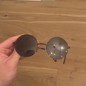 Runda svarta solglasögon i metall - Snygga solglasögon med rund form och svarta glas. Bågarna är tunna och i metall med näskuddar för extra komfort. Perfekt accessoar för en cool och retro look.