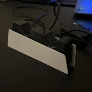 PlayStation 5 DualSense Charging Station - Laddstation för PlayStation 5 DualSense-kontroller. Rymmer två kontroller samtidigt och laddar dem snabbt och smidigt. Snygg vit och svart design som matchar PS5. Fint skick, inga synliga repor eller skador.