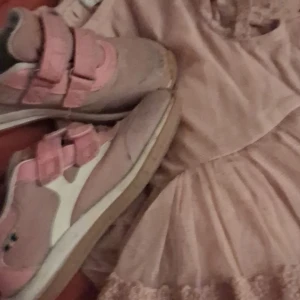 Rosa och vita sneakers med kardborre - Snygga sneakers i ljusrosa och vitt med två breda kardborreband. Skorna har en platt sula och rund tå, perfekt för en avslappnad och sportig look. Materialet är syntet och textil, vilket gör dem lätta och bekväma att bära. Fina kavatskor storlek 26 