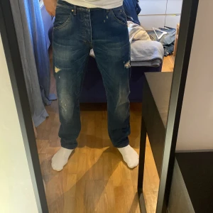 Tiger of Sweden blå jeans straight fit - Säljer ett par tiger of Sweden jeans i blå denim med slitna detaljer och raka ben. Jeansen har normal passform liknande Levis 501, fem fickor och knappar i gylfen. Perfekt för dig som gillar en avslappnad och tidlös look.