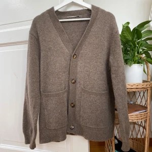 Beige kofta i lammull från A Day's March - Mysig beige kofta från A Day's March i 100% lammull. Modellen har v-ringning, knappar framtill och två stora fickor. Perfekt för lager-på-lager och chill höst- eller vinterstil.