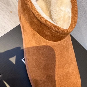 Bruna mockaboots med fårullsfoder - Mysiga boots i brun mocka med mjukt, ljust fårullsfoder på insidan. Skorna har en enkel och stilren design med rund tå och platt sula, perfekta för kalla dagar. Materialet är mocka på utsidan och insidan är fodrad med fluffig ull för extra värme.