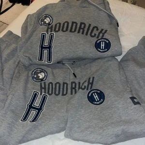 Grå hoodie från Hoodrich med patchar - Säljer en grå hoodie från Hoodrich med stora tryck och broderade patchar på bröstet. Tröjan har huva med dragsko och coola detaljer som ett stort H och texten 'Hoodrich' framtill. Perfekt för dig som gillar streetwear och vill sticka ut.