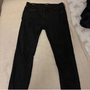 Svarta jeans från Jack & Jones - Svarta jeans från Jack & Jones i modellen Tapered/Mike. Jeansen har klassisk femficksdesign, normalhög midja och avsmalnande ben. Perfekta för dig som gillar en stilren och enkel look. 33W, 34L