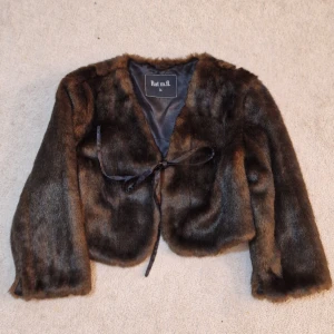 Brun pälsjacka från Rut m.fl. - Snygg croppad pälsjacka i mörkbrunt från Rut m.fl. Jackan har mjukt foder och knytband framtill. Perfekt för dig som vill ha en cool och lyxig look med vintagevibbar. Passar dig som gillar statement-plagg och vill sticka ut.