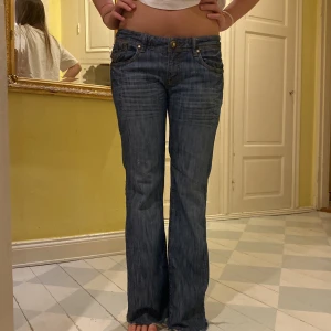 Blå bootcut jeans från Levis - Säljer ett par klassiska blå Levis jeans med bootcut passform och låg midja. Jeansen har fem fickor, slitna detaljer vid benslut och gylf med knapp. Tillverkade i tåligt denimtyg som ger en snygg vintagekänsla.