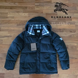Burberry Puffer - Svart dunjacka från Burberry med klassisk Säljer en elegant och mångsidig Burberry-jacka i svart, i nyskick. Dunfodrad för värme och komfort med det klassiska rutmönstret i huvan som ger en exklusiv touch. Praktiska dragkedjefickor, avtagbar huva och diskret logopatch på ärmen. Jackan är i princip som ny och utan defekter. Passar L/M. En lyxig kombination av stil och funktion – perfekt för både vardag och tillfällen då du vill klä upp dig.  📦Snabb leverans - skickas samma dag📦 