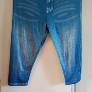 Blå croppade byxor med jeanslook XL - Säljer ett par blå croppade byxor i storlek XL med cool jeanslook och slitningar. Byxorna är tillverkade i stretchigt material av polyester och elastan, vilket gör dem riktigt bekväma. Perfekta för dig som gillar avslappnad stil med denimkänsla.