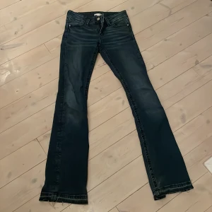 Mörkblå bootcut jeans Gina Tricot - Snygga mörkblå jeans från Gina Tricot i bootcut-modell. Jeansen har klassisk femficksdesign, markerade sömmar och slitna detaljer vid bensluten. Bakfickorna har lock och knapp. Perfekta för dig som gillar en tidlös look med lite edge.