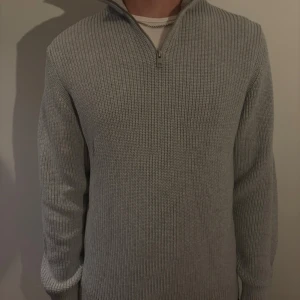 Grå stickad half zip-tröja från Zara - Säljer en grå stickad tröja från Zara med half zip och hög krage. Clean och stilren look. Perfekt för lager-på-lager och funkar året runt när du vill vara både chill och snygg. Aldrig använd!