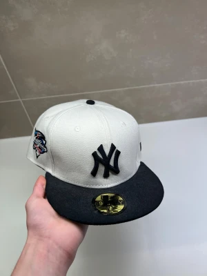 New Era Keps - Snygg New Era 59FIFTY keps med New York Yankees-logga framtill och World Series 2000 brodyr på sidan. Kepsen är vit med svart skärm och svarta detaljer. Tillverkad i bomull och har klassisk flat brim. Perfekt för dig som gillar streetwear och sport. Den är sprillans ny!!!