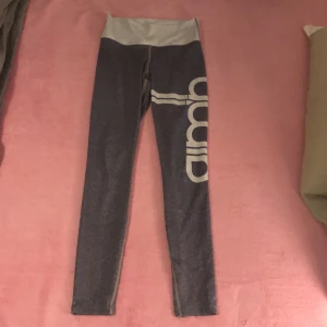 Gråa gympa byxor från aimin  - Snygga grå tights från Aimini i storlek XS med stort vitt tryck längs benet. Hög midja i ljusgrått och stretchigt material som består av polyester och spandex. Perfekta för träning, idrott eller chill, sitter tight och bekvämt. 