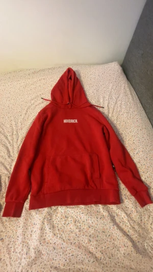 Röd hoodie från Hoodrich med huva - Säljer en röd hoodie från Hoodrich med vit logga tryckt på bröstet. Tröjan har huva med snörning, stor magficka och ribbade muddar vid ärmslut och nederkant. Perfekt för chill dagar och streetwear-stil.
