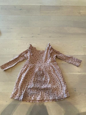 Blommig långärmad klänning Lindex 116 - Supersöt ljusrosa klänning från Lindex med små blommor i vinröda och rosa toner. Klänningen har lång ärm, volangdetaljer på axlarna och är sydd i mjuk, ribbad bomull. Perfekt för vår och sommar!